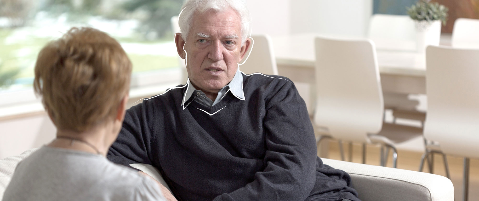 Zwei ältere Personen sitzen sich auf einer Couch gegenüber und unterhalten sich.